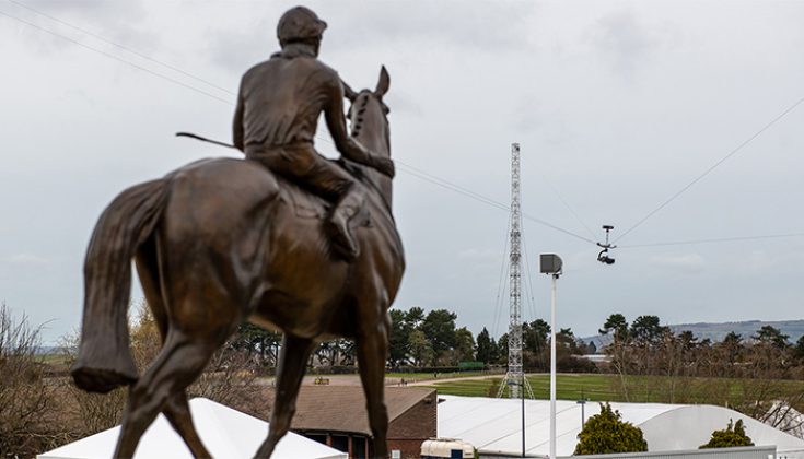 Close up of Jockey and Horse Statue at Cheltenham Racecourse. Background featuring Wirecam and Truss Tower for ITV Horse Racing at Cheltenham Festival 2022.