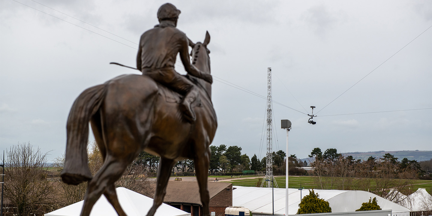 Close up of Jockey and Horse Statue at Cheltenham Racecourse. Background featuring Wirecam and Truss Tower for ITV Horse Racing at Cheltenham Festival 2022.