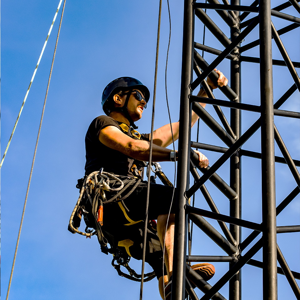 Rigger working at height, midway up a truss tower using a rope access solution.